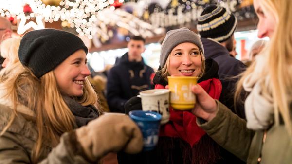 Freunde wärmen sich mit Glühwein auf einem Weihnachtsmarkt auf.