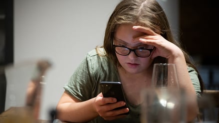 Eine junge Frau mit Downsyndrom schaut auf ihr Smartphone (Symbolbild).