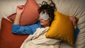 Eine schlafende junge Frau inmitten von Kissen (Symbolbild).