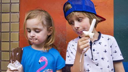 Cute siblings eating popsicles while standing against wall model released Symbolfoto JLOF00414