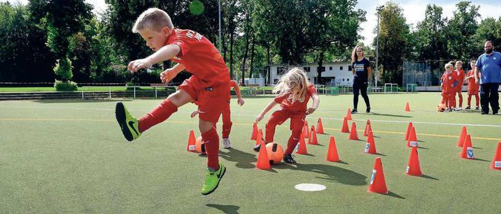 Jungen und Mädchen spielen Fußball beim Feriencamp in Lichterfelde. Im Hintergrund Trainerin Vicdan Yavas und Trainer Alexander Regh.