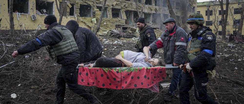 Ukrainische Rettungskräfte und Freiwillige tragen eine verletzte schwangere Frau aus einer Entbindungsklinik in Mariupol, die durch Beschuss beschädigt wurde.