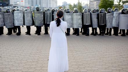 Eine Demonstrantin steht in Minsk Sicherheitskräften gegenüber. 