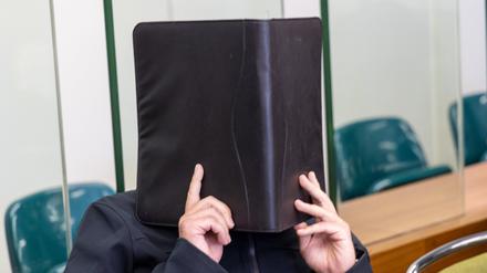 29.08.2022, Berlin: Einer der Angeklagten sitzt im Gerichtssaal des Kriminalgerichts Moabit hinter ihrern Anwälten und verdeckt sein Gesicht. Hier begann der Prozess gegen insgesamt fünf Männer. Die Berliner Generalstaatsanwaltschaft wirft ihnen unter anderen vor, spätestens im Januar 2017 beschlossen zu haben, Brandanschläge auf die Autos zweier Männer zu verüben, die sich politisch gegen Rechtsextremismus engagieren. In der Nacht zum 1. Februar 2018 sollen sie im Bezirk Neukölln die Autos angezündet und dadurch beschädigt haben. Die Vorwürfe lauten Bedrohung, Brandstiftung beziehungsweise Beihilfe dazu, Sachbeschädigung und Verwenden von Kennzeichen verfassungswidriger Organisationen. Mit der Anschlagsserie befasst sich auch ein parlamentarischer Untersuchungsausschuss des Berliner Abgeordnetenhauses. Foto: Christian Ender/dpa +++ dpa-Bildfunk +++