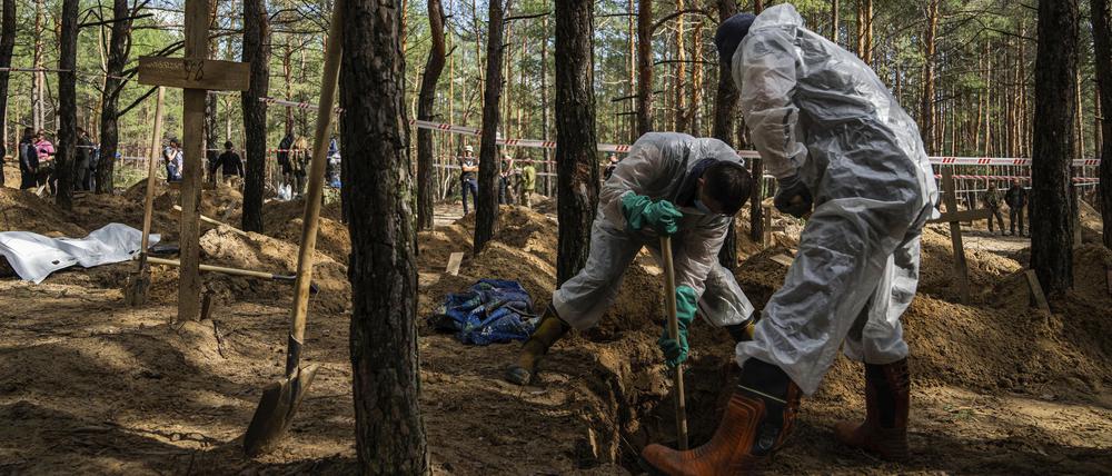 17.09.2022, Ukraine, Isjum: Zwei Arbeiter graben das Grab eines nicht identifizierten Zivilisten aus, zwischen anderen Gräbern ohne Namen von Zivilisten und ukrainischen Soldaten, während einer Exhumierung auf dem Waldfriedhof von Isjum, Ukraine.