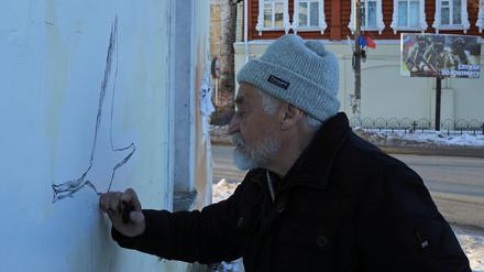 Der Künstler Wladimir Owtschinnikow malt ein Wandgemälde an einem Gebäude in der Nähe einer Tafel, die für den freiwilligen Militärdienst in den russischen Streitkräften wirbt.