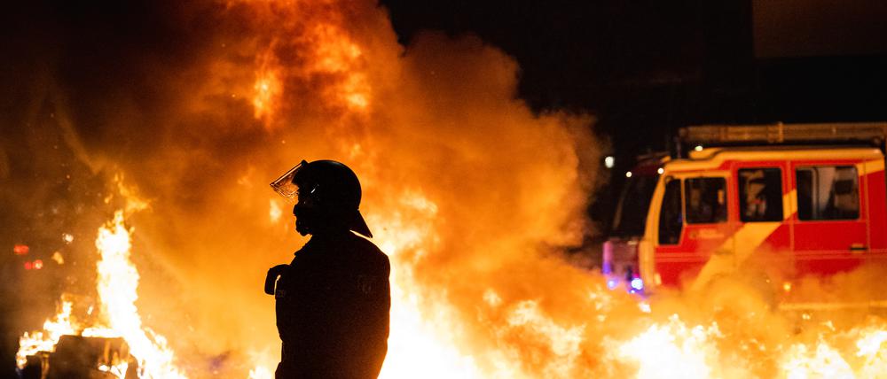 Ein Polizist steht vor einer brennenden Barrikade aus Mülltonnen und Mietrollern an der Kreuzung Urbanstraße.