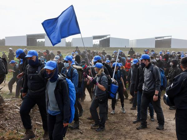 Demonstranten mit blauer Protestfahne am Werksgelände der Tesla-Fabrik Grünheide.