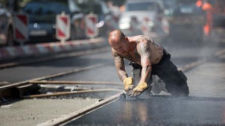 Bei sommerlichen Temperaturen bearbeitet ein Bauarbeiter heißen Teer an Gleisen einer Straßenbahnlinie.