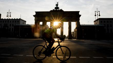 Ein Radfahrer fährt bei aufgehender Sonne am Brandenburger Tor vorbei. Strahlender Sonnenschein und sommerliche Temperaturen erwarten die Bewohner Berlins und Brandenburgs zu Beginn der Woche. 