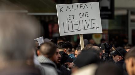 Teilnehmer einer Islamisten-Demo halten ein Plakat mit der Aufschrift „Kalifat ist die Lösung“ in die Höhe. 