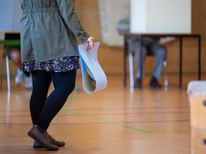 Eine wahlberechtigte Frau wartet in einem Wahllokal mit ihren Stimmzetteln in der Hand auf die Stimmabgabe.