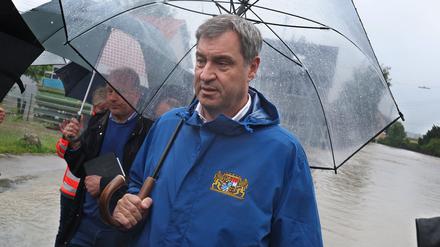 Markus Söder (CSU), bayerischer Ministerpräsident steht, umringt von Journalisten, am Rande einer überfluteten Straße. 