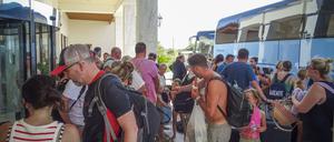 Touristen warten vor ihrem Hotel auf der griechischen Insel Rhodos auf den Einstieg in Busse.