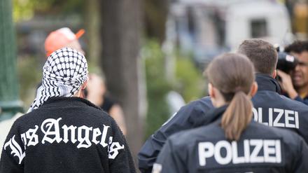 Polizeibeamte gehen im Stadtteil Neukölln neben einem Mann mit Palästinensertuch auf dem Kopf über den Richardplatz. 