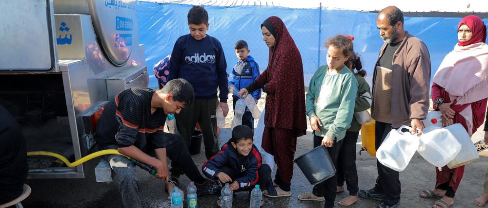 08.12.2023, Palästinensische Gebiete, Rafah: In einer provisorischen Unterkunft im südlichen Gazastreifen stehen die Menschen Schlange, um Wasser zu bekommen.