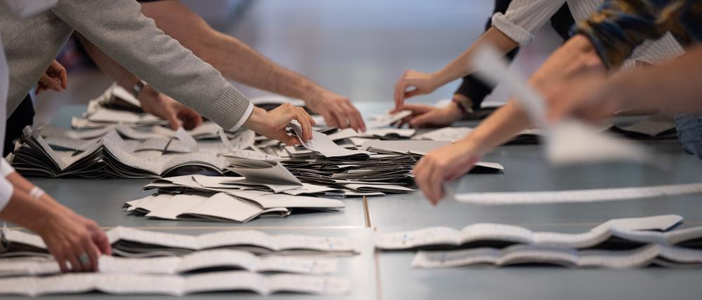 Wahlhelfer und Wahlhelferinnen zählen in einem Wahllokal Stimmzettel für die Bundestagswahl.