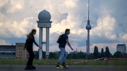 Zwei Inline-Skater fahren bei warmen Temperaturen vor der Kulisse des Berliner Fernsehturms über das Tempelhofer Feld. 