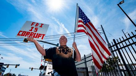 Ein Demonstrant hält in Massachusetts ein Schild und die amerikanische Flagge in die Höhe.