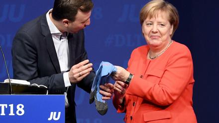 Zum Abschied schenkt der Vorsitzende der Jungen Union (JU), Paul Ziemiak, Merkel ein Paar Socken.
