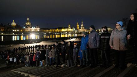 Teilnehmer der Menschenkette stehen am Mittwoch am Ufer der Elbe Hand in Hand.