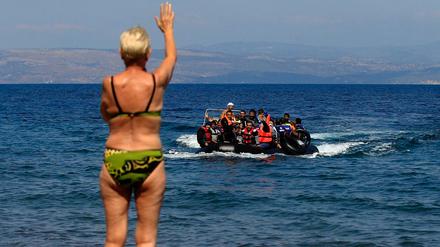 Ein Badegast winkt Flüchtlingen aus Syrien zu, die aus der Türkei mit einem Schlauchboot an die Küste von Mitilini auf der Insel Lesbos kommen. 