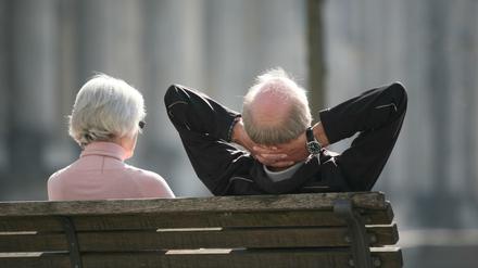 Ein Rentnerpaar sitzt auf einer Bank vor dem Reichstag und sonnt sich.