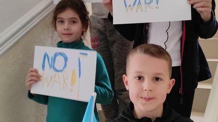Kinder einer Kiewer Familie halten im Treppenhaus "No War"-Schilder in die Kamera.