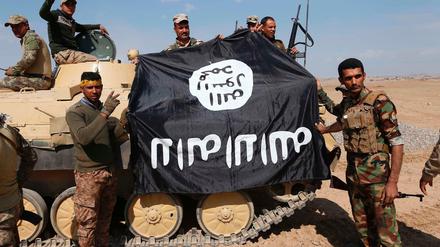 Irakische Soldaten halten eine erbeutete IS-Fahne hoch.