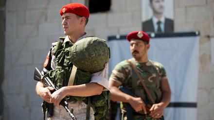 Russische und syrische Militärpolizisten stehen Wache vor einem Porträt des syrischen Präsidenten al-Assad. 