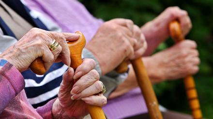 Senioren sitzen in Leichlingen mit Gehstöcken auf einer Parkbank. 