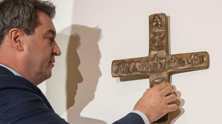 Markus Söder, Bayerischer Ministerpräsident (CSU), hängt ein Kreuz im Eingangsbereich der bayerischen Staatskanzlei auf. 