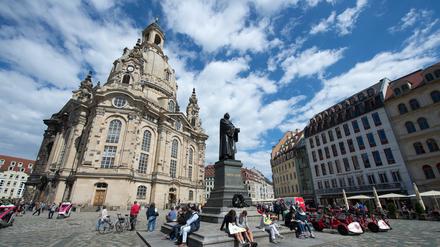 Vor dem Martin-Luther-Standbild auf dem Neumarkt in Dresden (Sachsen) rasten am Touristen, links die Frauenkirche.