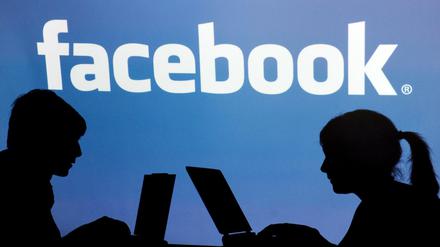 Die Schatten von Jugendlichen mit einem Laptop sind vor dem Schriftzug des sozialen Internet-Netzwerks Facebook zu sehen.