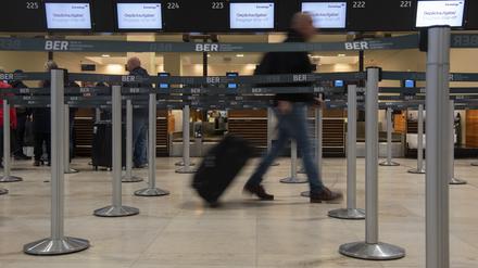 Ein Reisender geht am Flughafen BER mit einem Koffer zu einem Check-in-Schalter von Eurowings. 