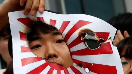 Ein Mann hält ein brennendes Bild der japanischen "Flagge der aufgehenden Sonne" während einer Kundgebung in Seoul. 