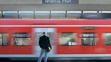 Ein Mann steht an einem Mainzer Bahnsteig, an ihm fährt gerade ein roter Regionalzug vorbei.