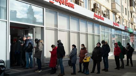 Menschen stehen in einer Schlange, um Geld von einem Geldautomaten der Alfa Bank in Moskau abzuheben.