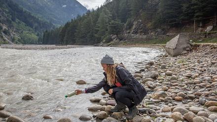Die Forscherin Emily Duncan hockt an einem Flussufer und lässt eine Plastikflaschenpost ins Wasser.
