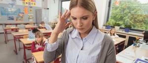 Eine gestresste junge Grundschullehrerin wendet sich mit Kopfschmerzen von der Klasse ab.