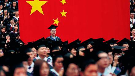 Hochschul-Absolventen in China feiern ihren Abschluss mit Doktorhüten auf dem Kopf - und vor einer überdimensionalen chinesischen Fahne.
