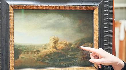 Das Rembrandt-Gemälde Landschaft mit Bogenbrücke - mit einer weiblichen Hand, die auf das Bild weist.