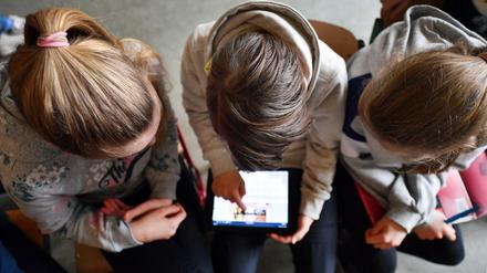 Drei Schüler beugen sich über einen Tablet-Computer.